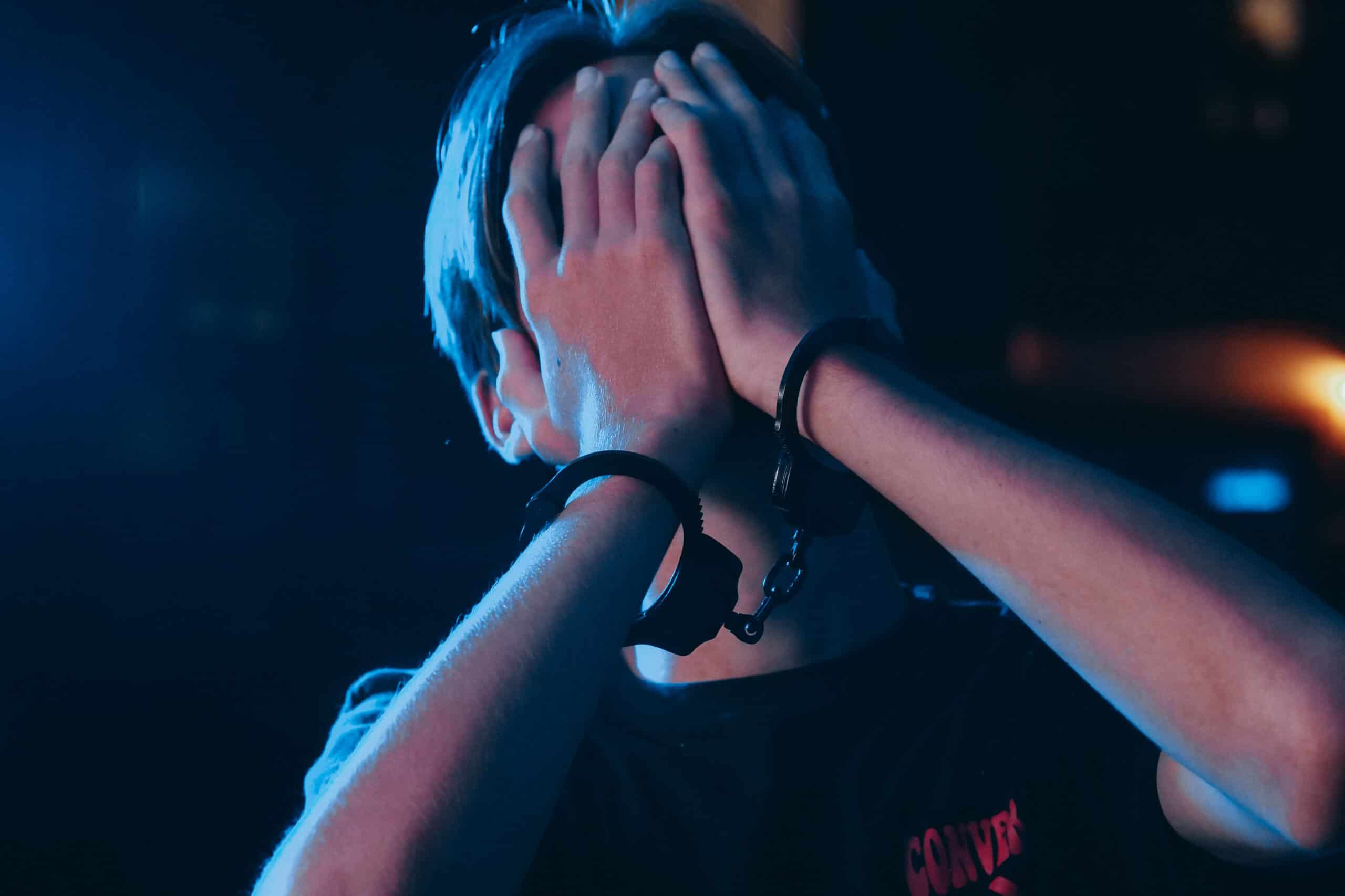 A boy with handcuffs and hands over his face